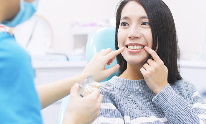 歯科医院スタッフに説明を受け、自分の歯を指さす女性