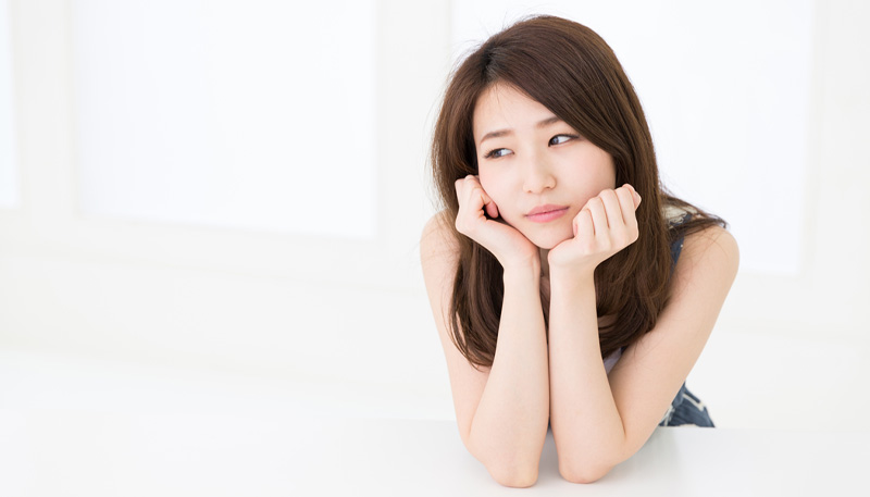 両手で頬杖をつき悩んでいる様子の女性