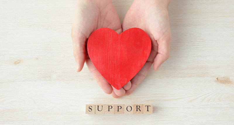 SUPPORTと書かれた期のブロックの近くで両手で優しく赤いハートを持つ写真