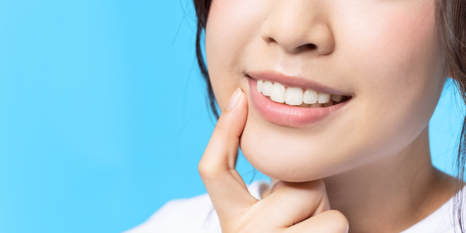 人差し指を白く綺麗な歯に当てて微笑む女性