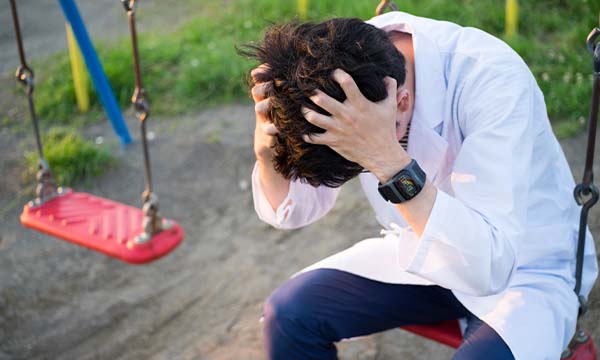 公園のブランコに座り、頭を抱えうつむく人