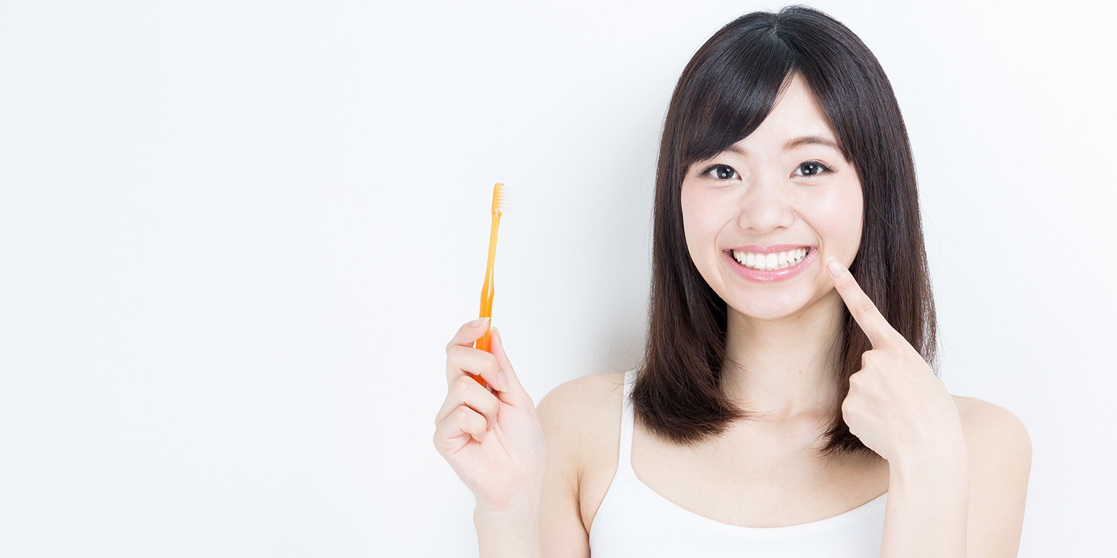 歯ブラシを持ち、自信の白い歯を指さす微笑んだ女性