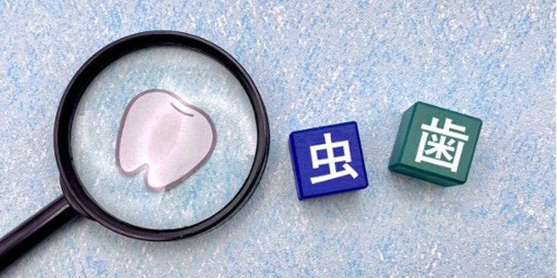 虫眼鏡の先に歯のイラスト、横に虫歯の文字