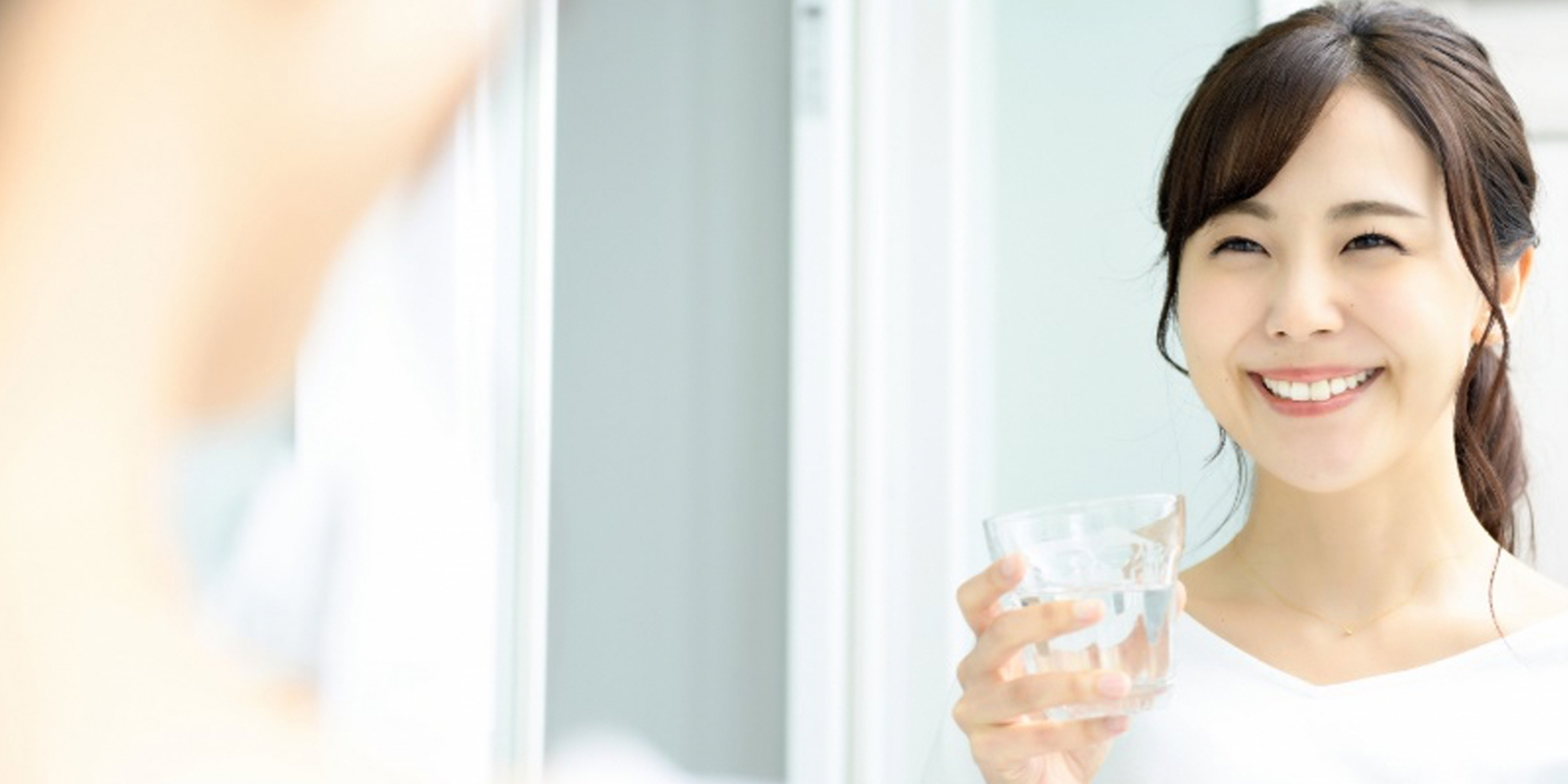 水の入ったコップを持ち、鏡に向かって微笑む女性