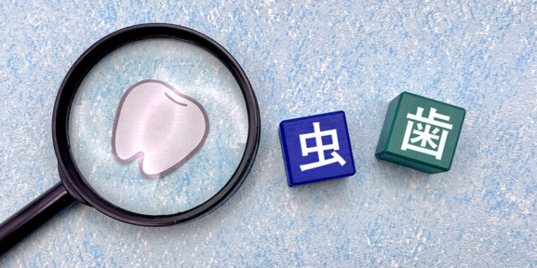 虫眼鏡の先に歯のイラスト、横に虫歯の文字