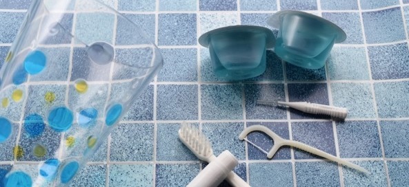 コップと歯ブラシと歯磨き粉、柄付き糸ようじとマウスウォッシュの口腔ケア用品の写真