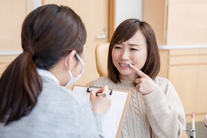 問診をとる女性スタッフと、顔を歪ませて口元を指さす女性患者